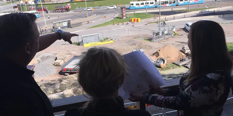 Tre personer i siluett som står på en höjd och tittar ut över ett arbetsområde