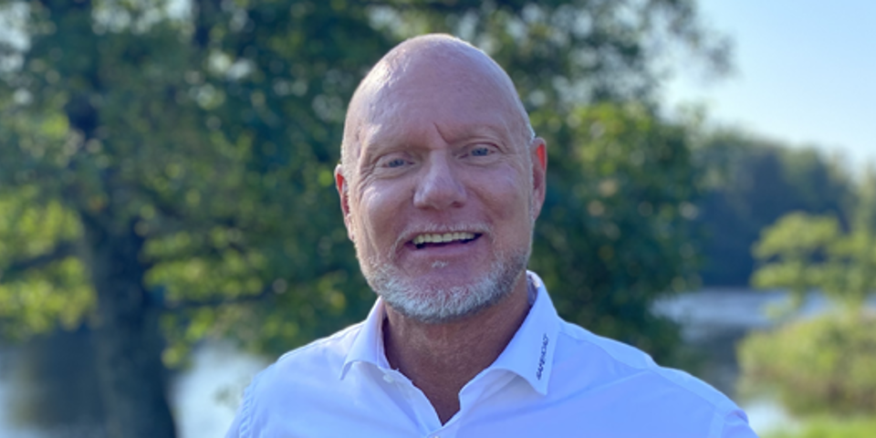 Person i vit skjorta som står framför ett träd en solig sommardag