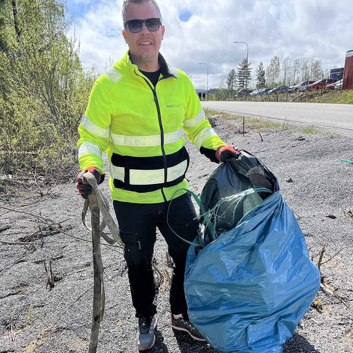 Man i varselkläder plockar skräp i naturen och lägger i en blå sop-påse