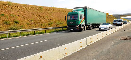 Skyddsbarriär i betong delar ett körfält i två delar på en väg med lastbild och personbil