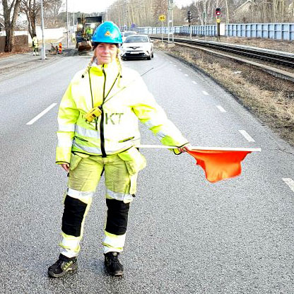 Bild på kvinna som håller en vaktflagga på en trafikerad väg