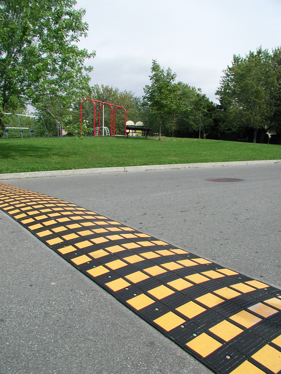 Bild på ett gult/svart farthinder som ligger på en asfalterad väg.