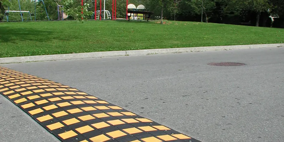 Bild på ett gult/svart farthinder som ligger på en asfalterad väg.